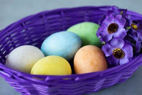 Five multicolored decorative eggs in a purple basket on a gray background. Ea Stock Photos