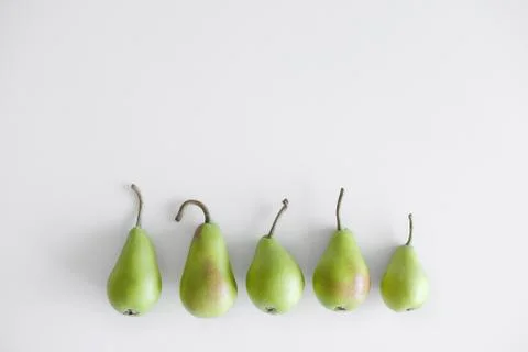 Five objects of green pears with twigs lie in a row on a white background Stock Photos