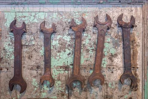 Five old, rusted wrench tools hanging on nails on cracked, damaged wall. Stock Photos