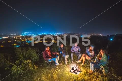 The five people sit near the bonfire on the background of the city. night tim Stock Photos