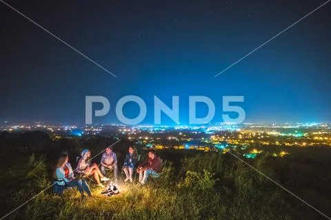 The five people sit near the bonfire on the background of the city. night tim Stock Photos
