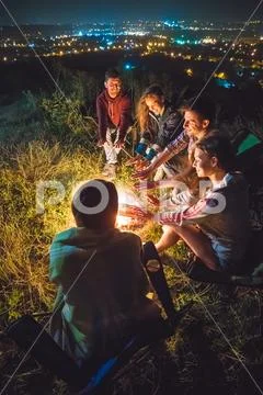 The five people sit near the bonfire on the background of the city. night tim Stock Photos