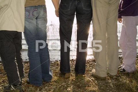Five people standing at lake shore, rear view, low section Stock Photos