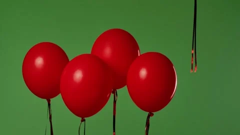 Five red helium balloons hang in the air on ribbons, and one floats upward Stock Footage 318779594
