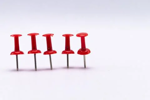 Five Red Push Pins Standing in a Row on a White Surface, Office Supplies. Stock Photos