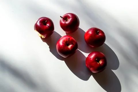 Five red ripe apples lying on a white table and their shadows Stock Photos