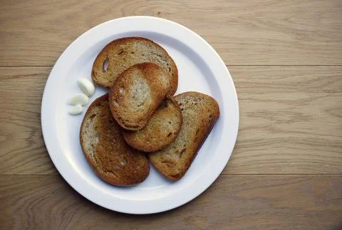 Five slices of fried bread with peeled garlic on white plate Stock Photos
