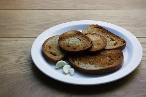Five slices of fried bread with peeled garlic on white plate Stock Photos