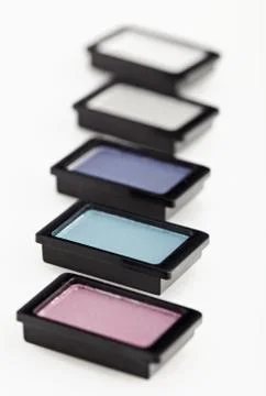 Five small multicolored eye-shadows arranged in line on white Fotos Stock