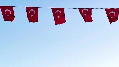 Five Small Turkish Flags  Hanging on a Wire Against a Light Blue Sky Stock Footage 322997432
