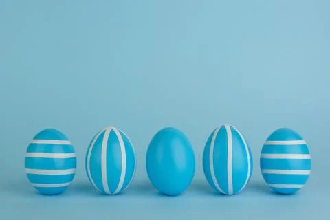 Five striped Easter blue eggs in a row on a blue background. Stock Photos