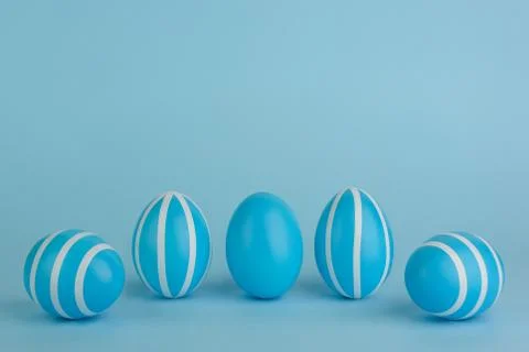 Five striped Easter blue eggs in a row on a blue background. Stock Photos