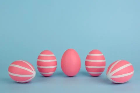 Five striped Easter pink eggs in a row on blue background. Copy space. Stock Photos
