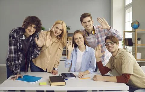 Five students are sitting at the table in the classroom and waving their hands Foto stock