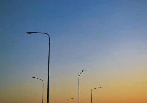 Five tall lampposts against a gradient evening clear sky at sunset Foto stock