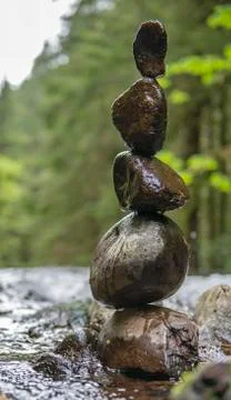 Five wet rocks stacked and balancing on top of one another near a flowing riv Stock Photos