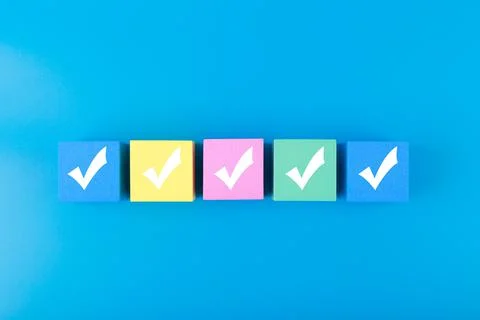 Five white checkmarks on multicolored cubes in a row against blue background Stock Photos