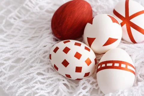 Five white Easter eggs with red geometric patterns on mesh textile net Stock Photos