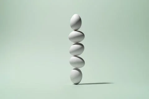 Five white eggs are balanced in a tall stack on a pastel green background. Photos