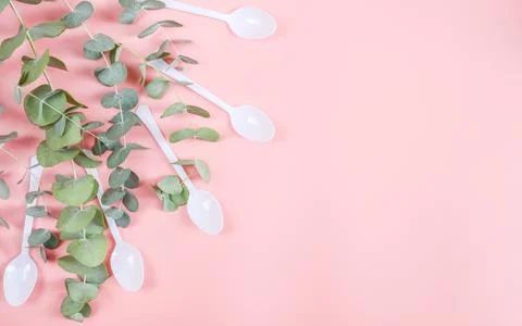 Five white plastic spoons with green branches lie on the left on a pink Stock Photos