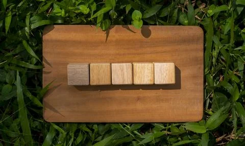 Five Wooden Cubes Arranged on Rustic Board Surrounded by Green Nature Stock Photos