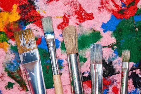 Five worn out brushes of different sizes on the colorful pink palette Stock Photos
