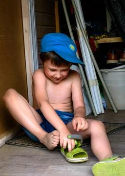 Five year old boy on the floor puts his sandals on his feet Stock-Fotos