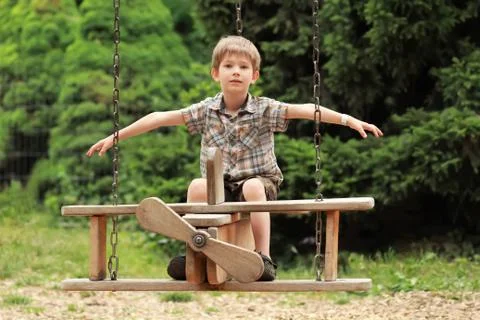 Five year old boy flying on a wooden biplane swing in the summer park Stock Photos