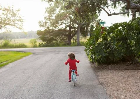 A five year old boy in a red shirt riding his bike on a quiet residential Stock Photos