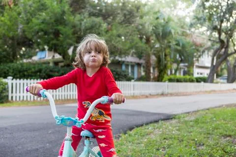 A five year old boy in a red shirt riding his bike on a quiet residential Stock Photos