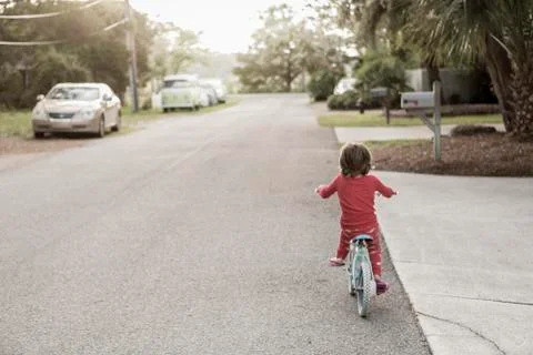 A five year old boy in a red shirt riding his bike on a quiet residential Stock Photos