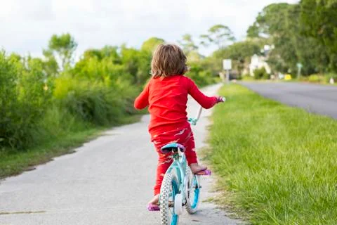 A five year old boy in a red shirt riding his bike on a quiet residential Stock Photos