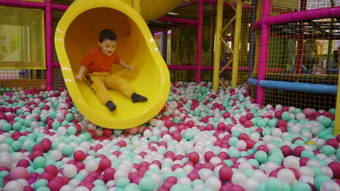 A five-year-old boy rolls down a tube slide and falls into inflatable balloons. Stock Footage 169395058