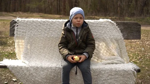 A five-year-old boy sits on a Park bench and eats an Apple,slow-mo Stock Footage 129090795