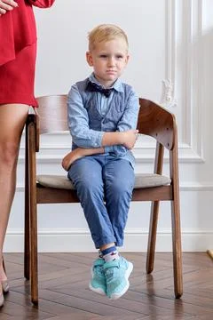 Five-year-old child sits on a chair with his hands folded cross on the cross Stock Photos