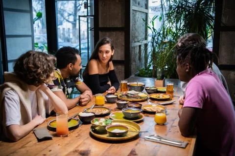 Five young friends sitting at the table in a cafe, chatting, hav Stock Photos