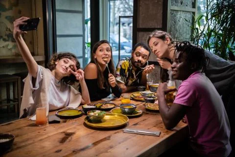 Five young friends sitting at the table in a cafe, taking selfie Stock Photos
