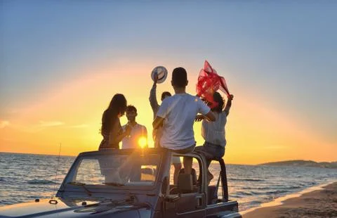 Five young people having fun in convertible car at the beach at sunset Stock Photos