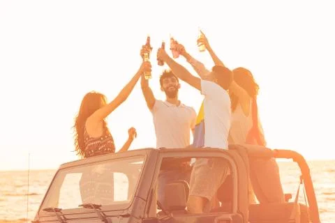 Five young people having fun in convertible car at the beach at sunset Stock Photos