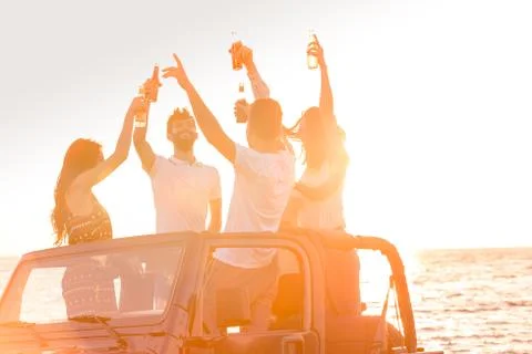Five young people having fun in convertible car at the beach at sunset Stock Photos
