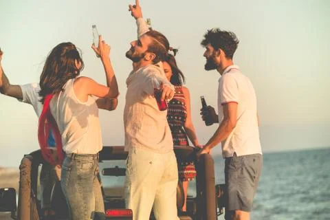 Five young people having fun in convertible car at the beach at sunset Stock Photos