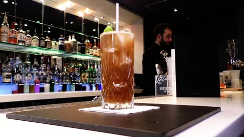 Fixed mid shot of Long Island Iced Tea cocktail with bar man in the background Stock Footage 106519330