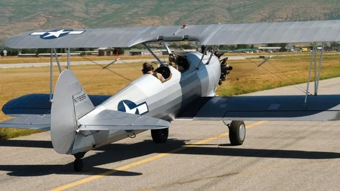 Fixed wing single engine retro biplane with two pilots is turning on runway Stock Footage 115953012