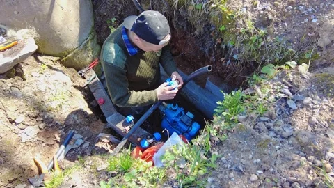Fixing a water pump in a hole in the ground in a backyard Stock Footage 337431729