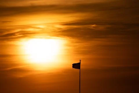 Flag flying at sunset with warm orange sky Stock Photos