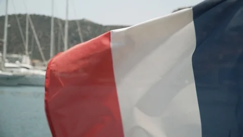 The flag of France develops in wind against backdrop of sea and moored yachts Stock Footage 113226711