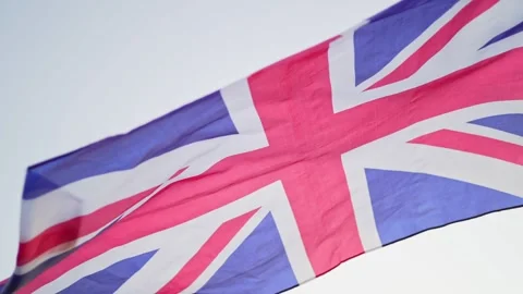 The flag of Great Britain develops in the wind at sunset against the sky. Slow Stock Footage 141989836