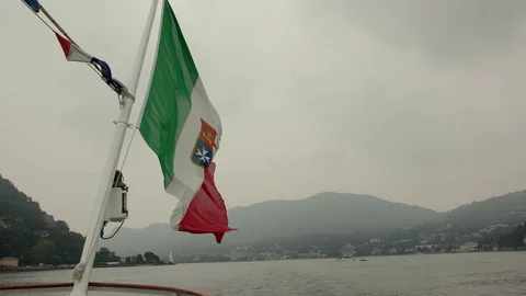 Flag of Italy develops against the backdrop of mountains in a haze on Lake Como Stock Footage 129043391