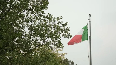 The flag of Italy, which is slightly torn, develops in the wind against the sky Stock Footage 128054994