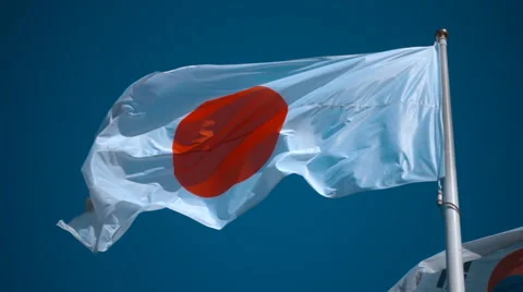 Flag of Japan on the flagpole waving in the wind against a blue sky Stock Footage 64723312